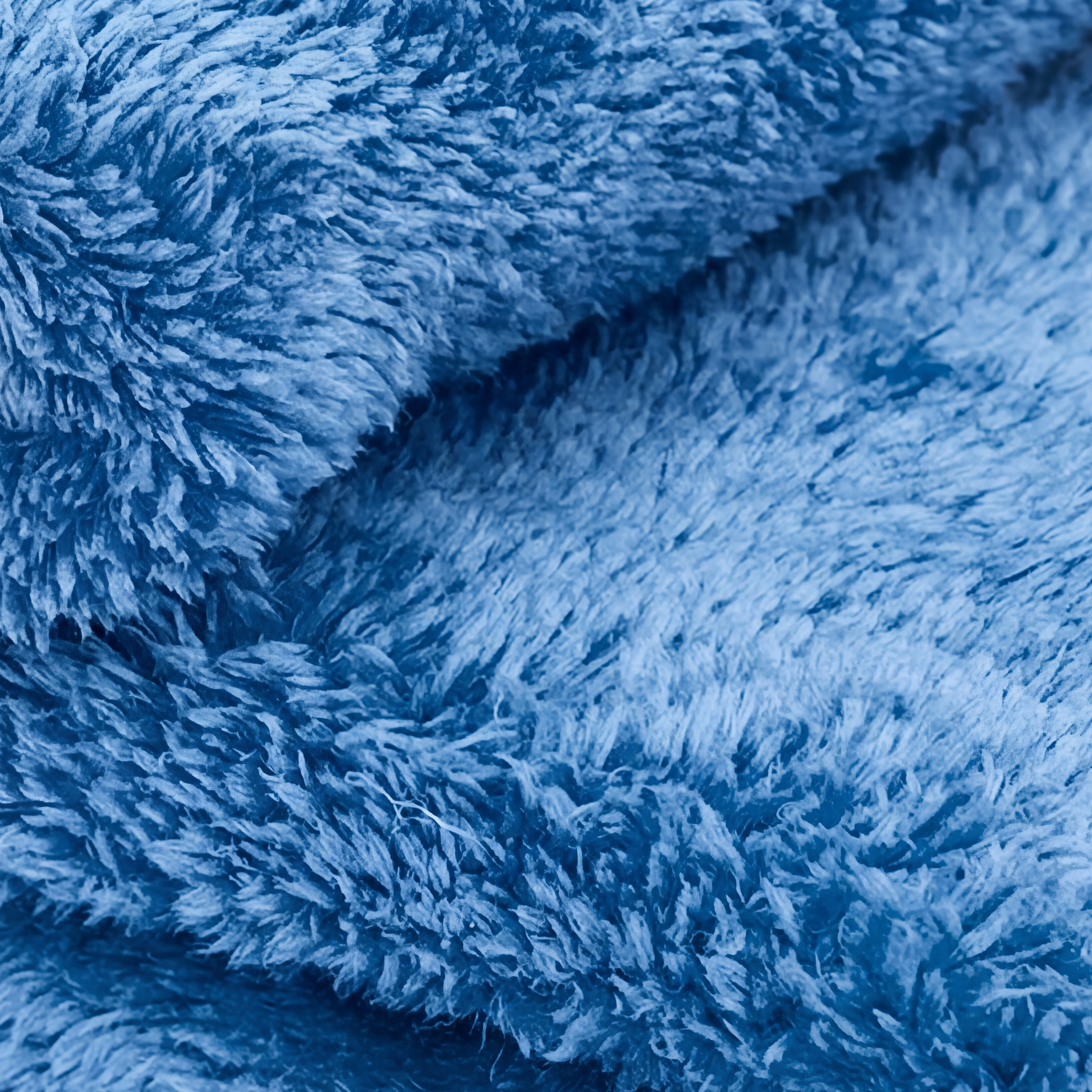 Close-up of a blue, plush fabric towel with a thick, shaggy texture and soft fibers.